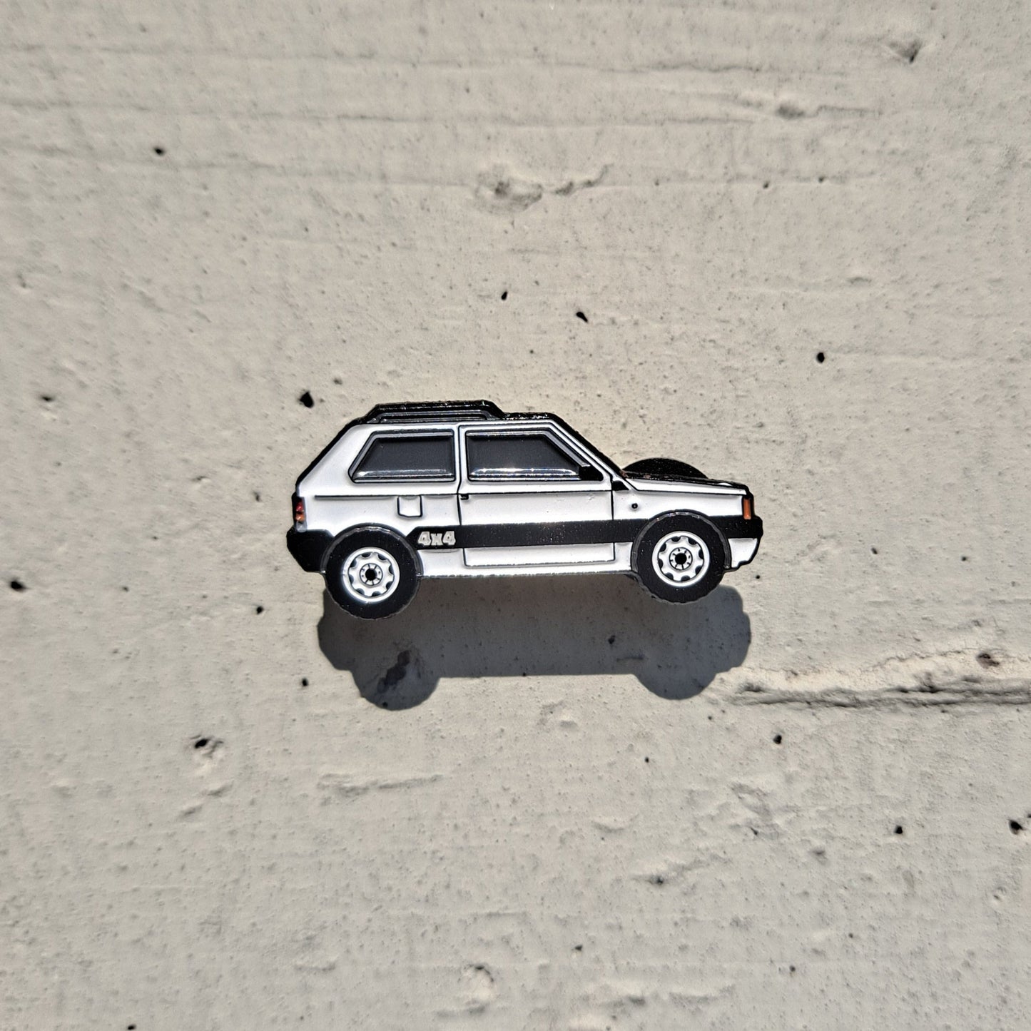Fiat Panda 4x4 white enamel pin on cement background