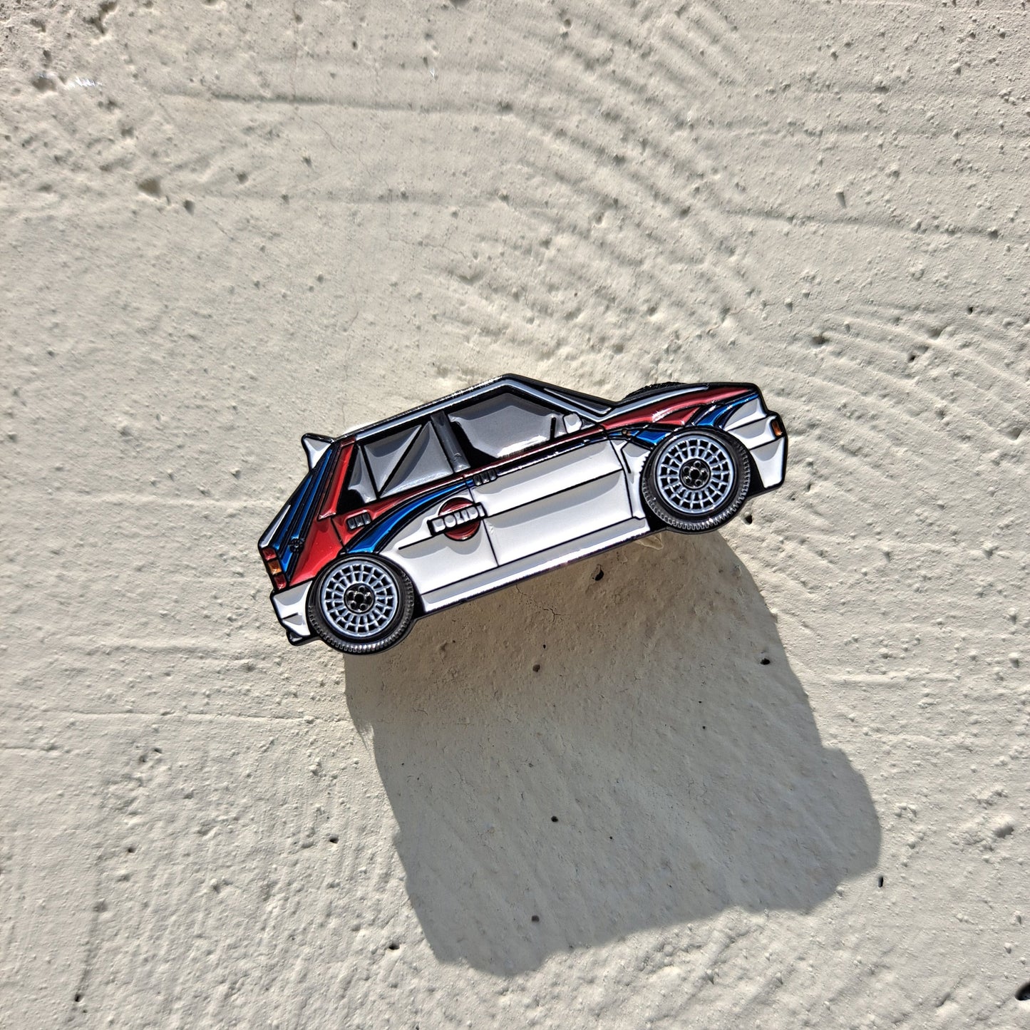 Lancia Delta Martini enamel pin on cement background