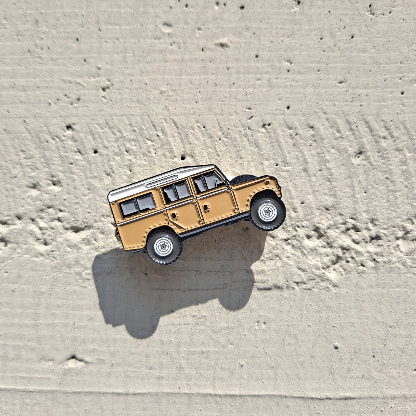 Land Rover Defender sand enamel pin on cement background